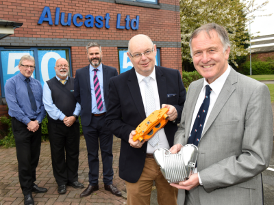 Five men in suits standing outside a brick building with corporate signage saying 'Alucast Ltd'