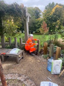 A man wearing orange work clothes and a hard hat kneeling down, working in the Dartmouth Park sensory garden