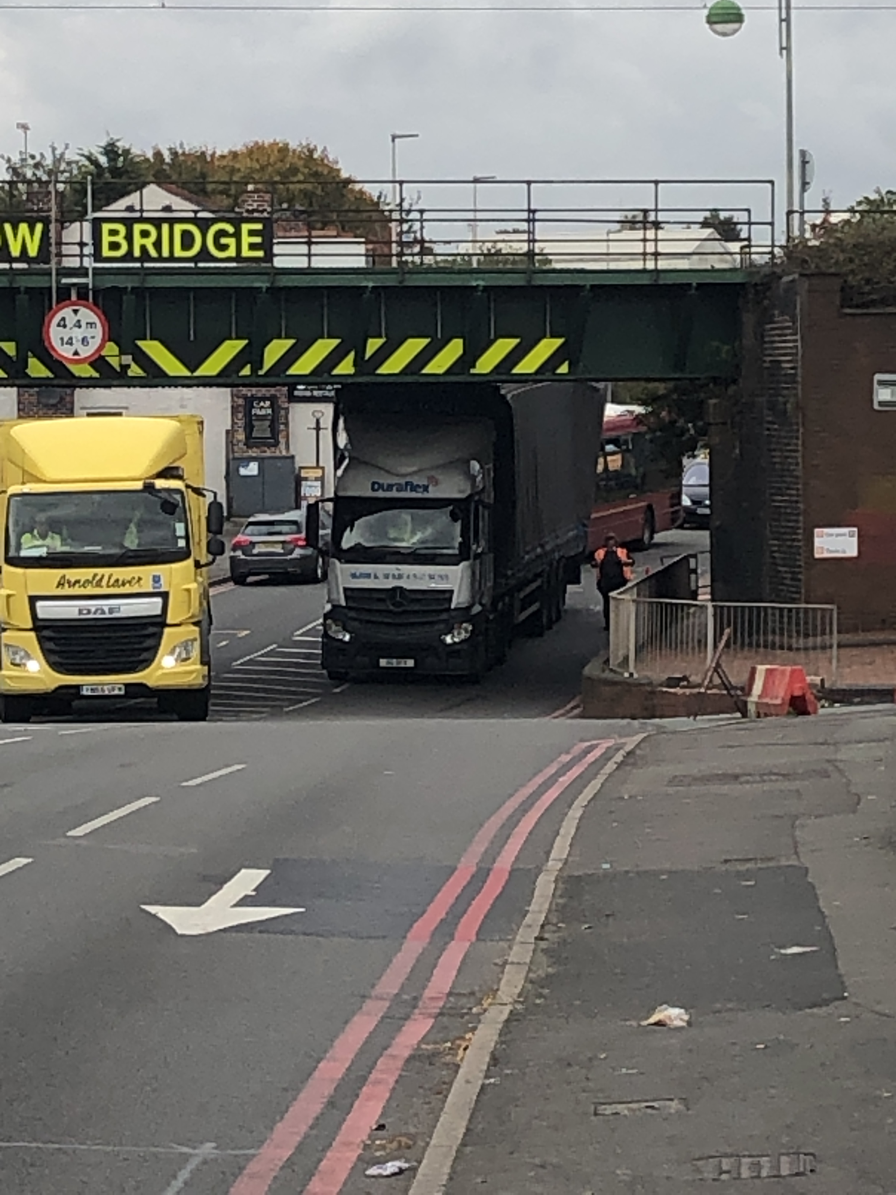 Two lorries passing under a low metal bridge.