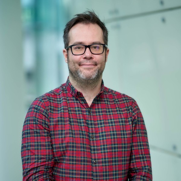 Head and shoulders shot of Chris Jones smiling, wearing a red checked shirt and black glasses