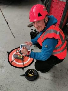 A person wearing a red hard hat and high vis vest bending down with a drone.