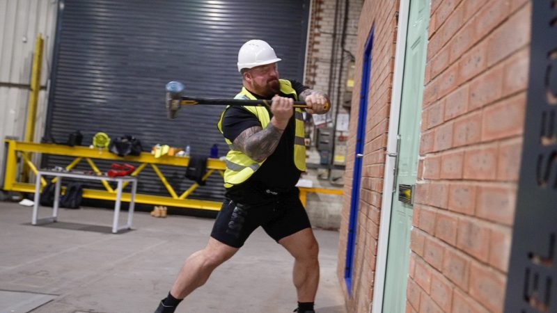 Eddie Hall with a hard hat and large sledge hammer attempts to break steel door.