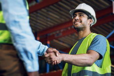 Workman wearing high-vis yellow jacket and hard hat shaking hands with another person