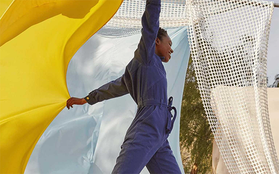 A person in a blue boiler suit holding some yellow fabric with white fabric in the background