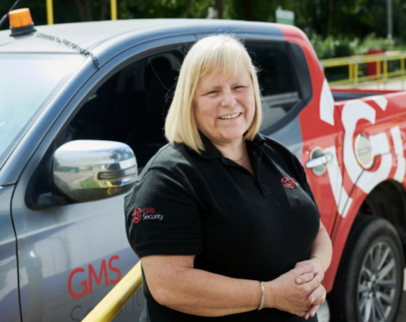 A female security officer in a black tshirt standing next to a GMS Security truck.