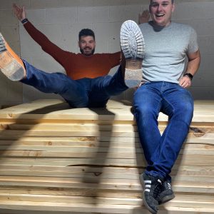 Sam Moseley and Rhys York of Grain and Frame sitting on a pile of wood