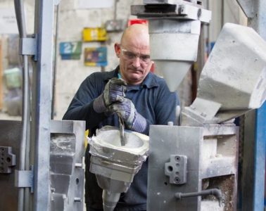 A worker in blue overalls working a die casting machine.