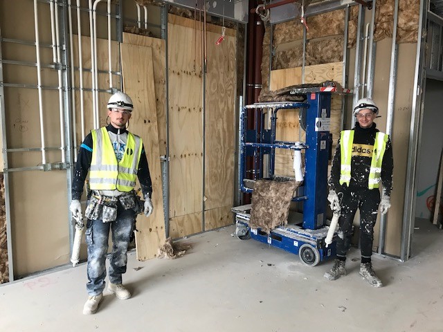 Two apprentices wearing hard hats, work boots and high vis jackets on a construction site