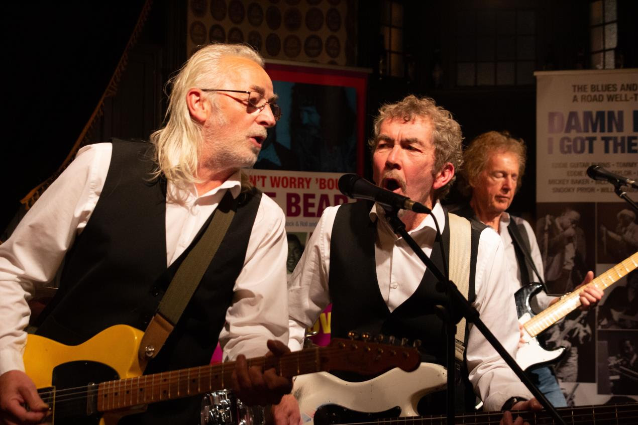 Three musicians on a stage playing guitars and singing