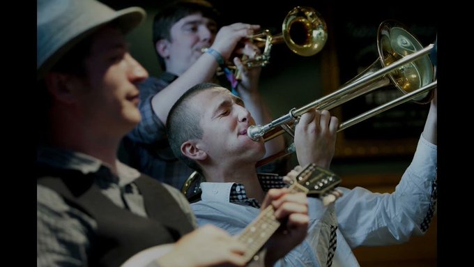 A still from a video showing a musicians playing a guitar, a trumpet and a trombone