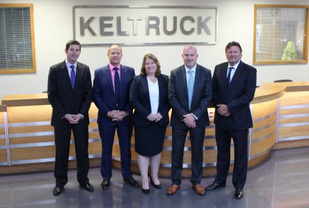 Five people in suits standing in front of a Keltruck logo on the wall 