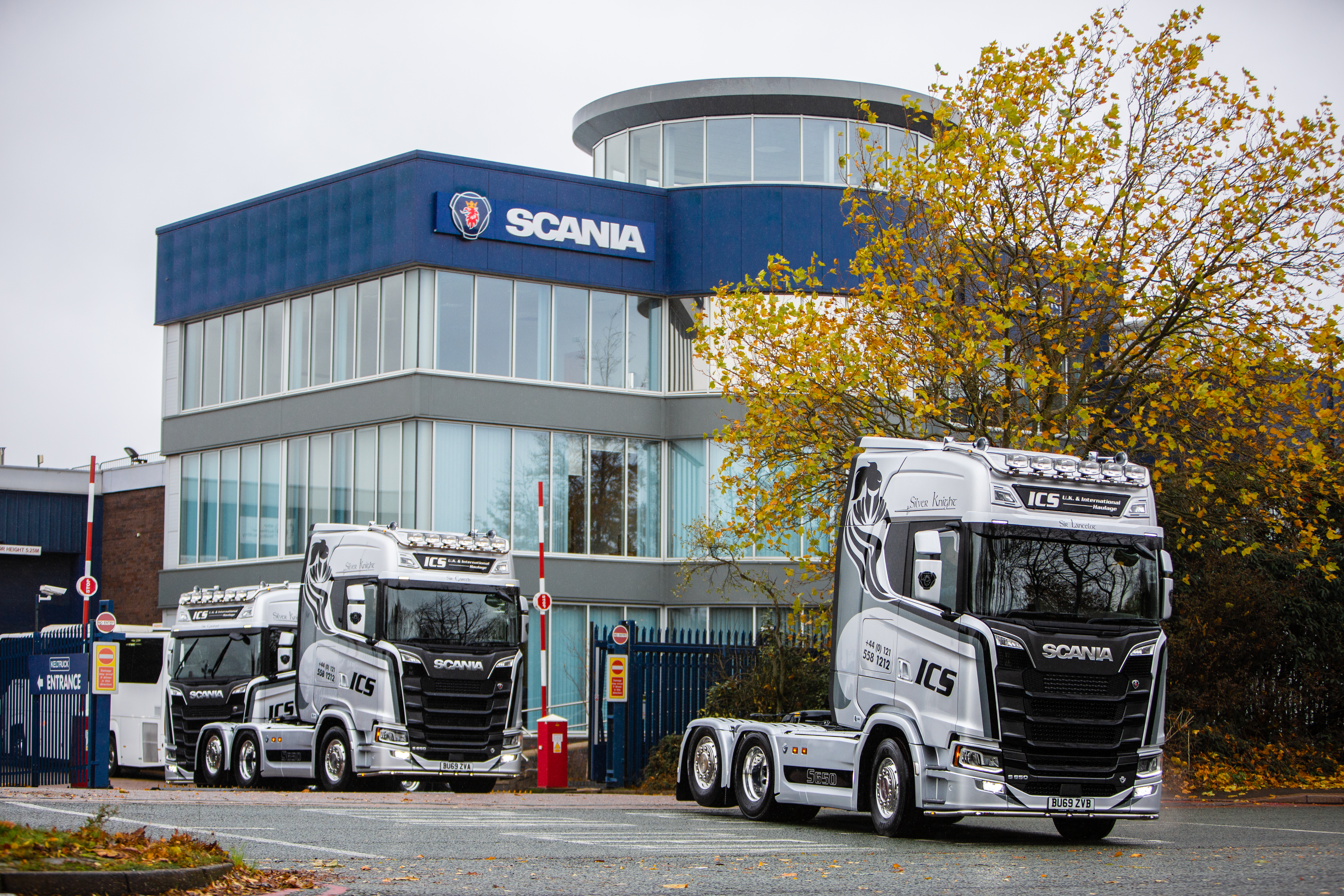 Two Scania lorries driving away from a building with a Scania logo on it