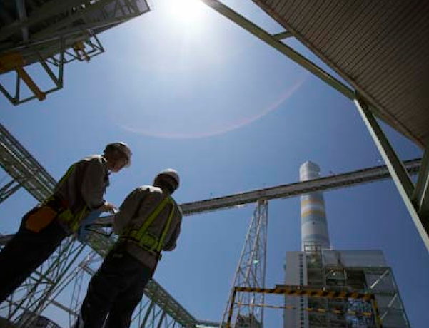 Two people in protective wear stand talking at an industrial site.