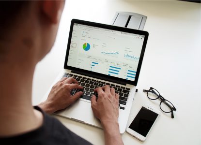 Close up of person's neck and hands on a laptop with a mobile phone and spectacles next to it