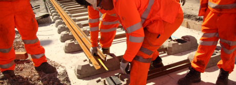 A close up of workers wearing orange high-vis PPE suits working on a railway track.