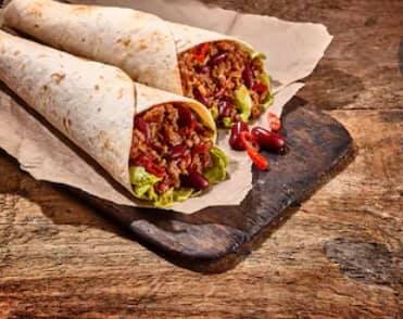 Two barbecue chicken wraps lying side by side on a wooden board, on a wooden table