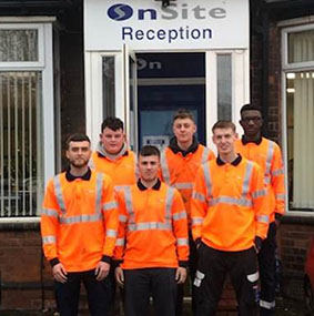 Six people wearing orange work jackets standing outside a building with an OnSite sign above them