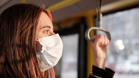 Young woman in a face mask holding a grab rail on a bus