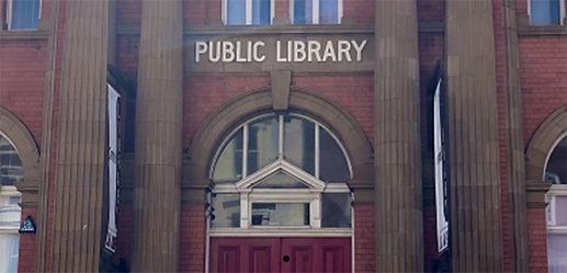 Close up of a red brick building with a sign above the door saying Public Library