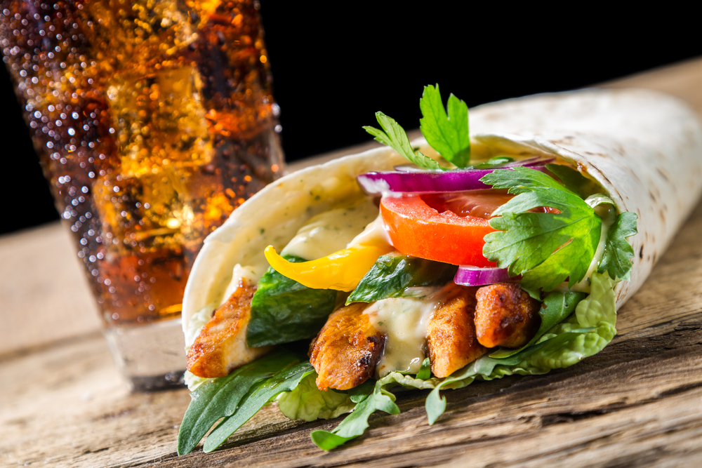 Fresh salad in a tortilla wrap next to a glass of cola on a wooden table