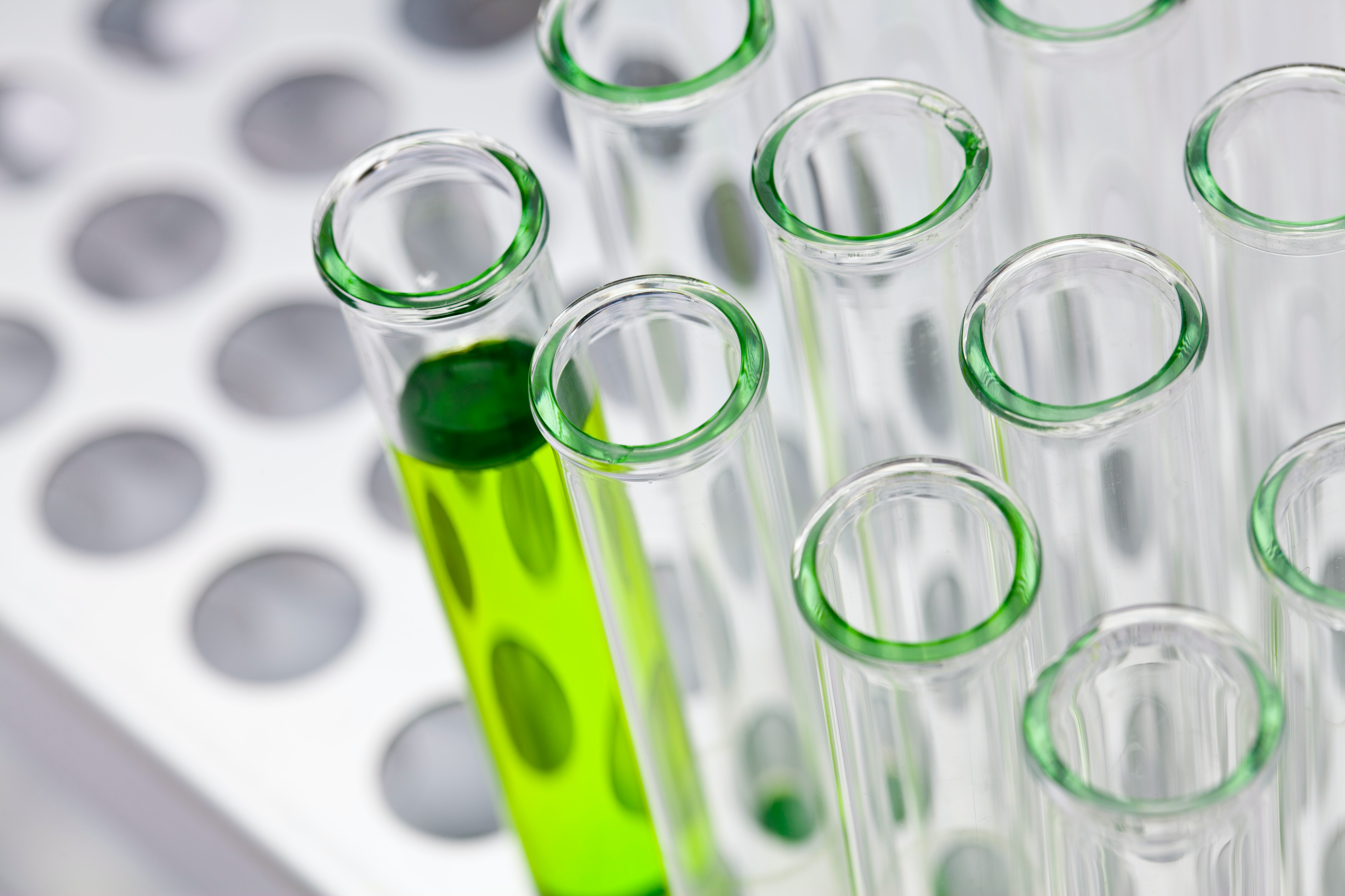 A close up of some test tubes in a rack with green liquid in one test tube.