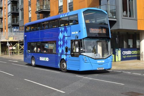 A blue double decker bus on a road outside an apartment building