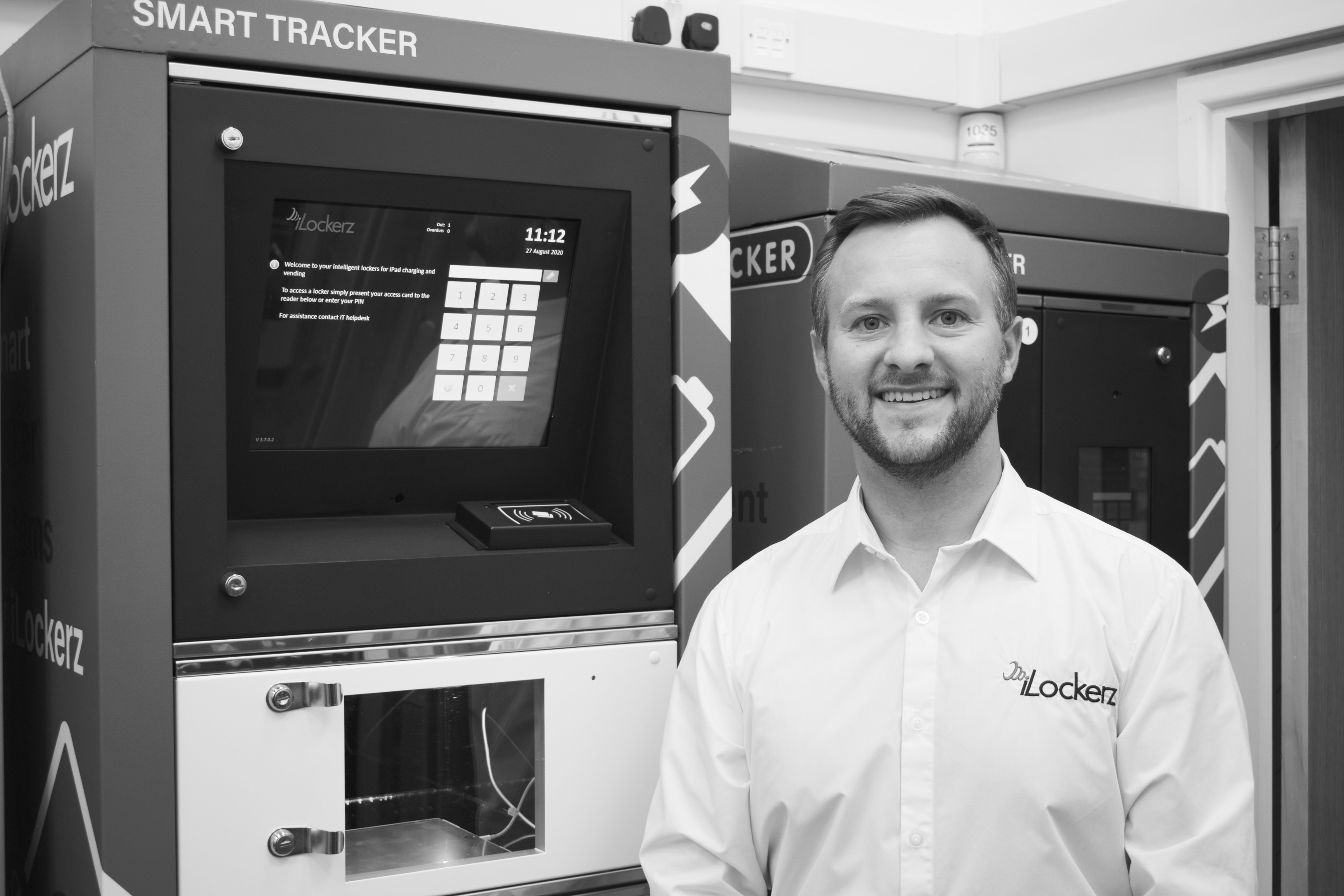 A black and white photo of a man standing infront of an iLockerz intelligent locker system