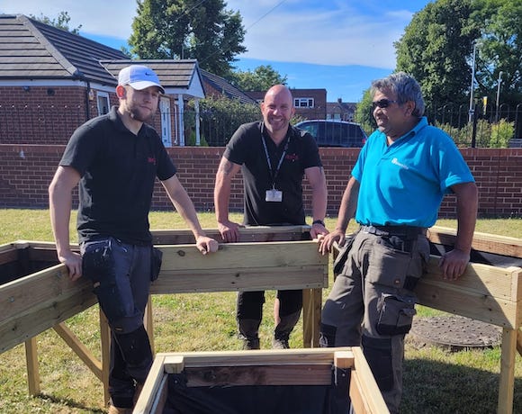 Three men stand outside leaning on wooden planters