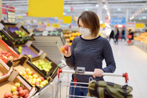 Young woman with a trolley in the produce section of a supermarket, wearing a face covering