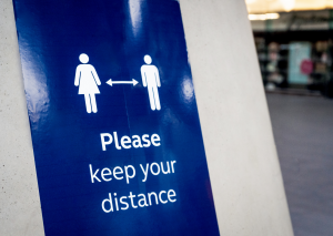 A blue sign with the text "Please keep your distance" and a male and female symbol in white with an arrow in between them