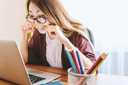 Woman wearing glasses biting a pencil looking at a laptop