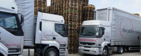 Three Pallet Company lorries parked infant of a tall stack of wooden pallets.