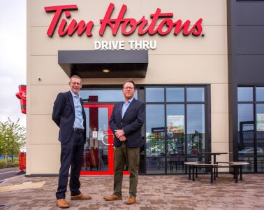 Two men in suits stand outside a branch of Tim Hortons, looking at the camera.