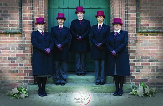 Five female funeral directors wearing purple top hats