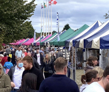 A photograph of market stalls with tented roofs and potential customers walking past