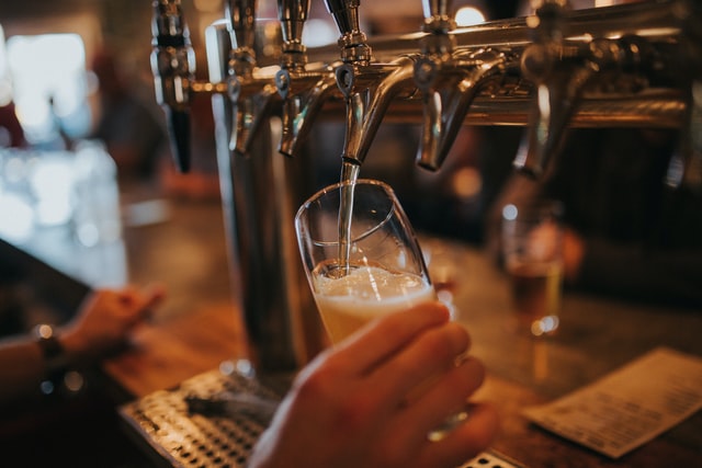 A hand pouring a glass of beer from a beer tap