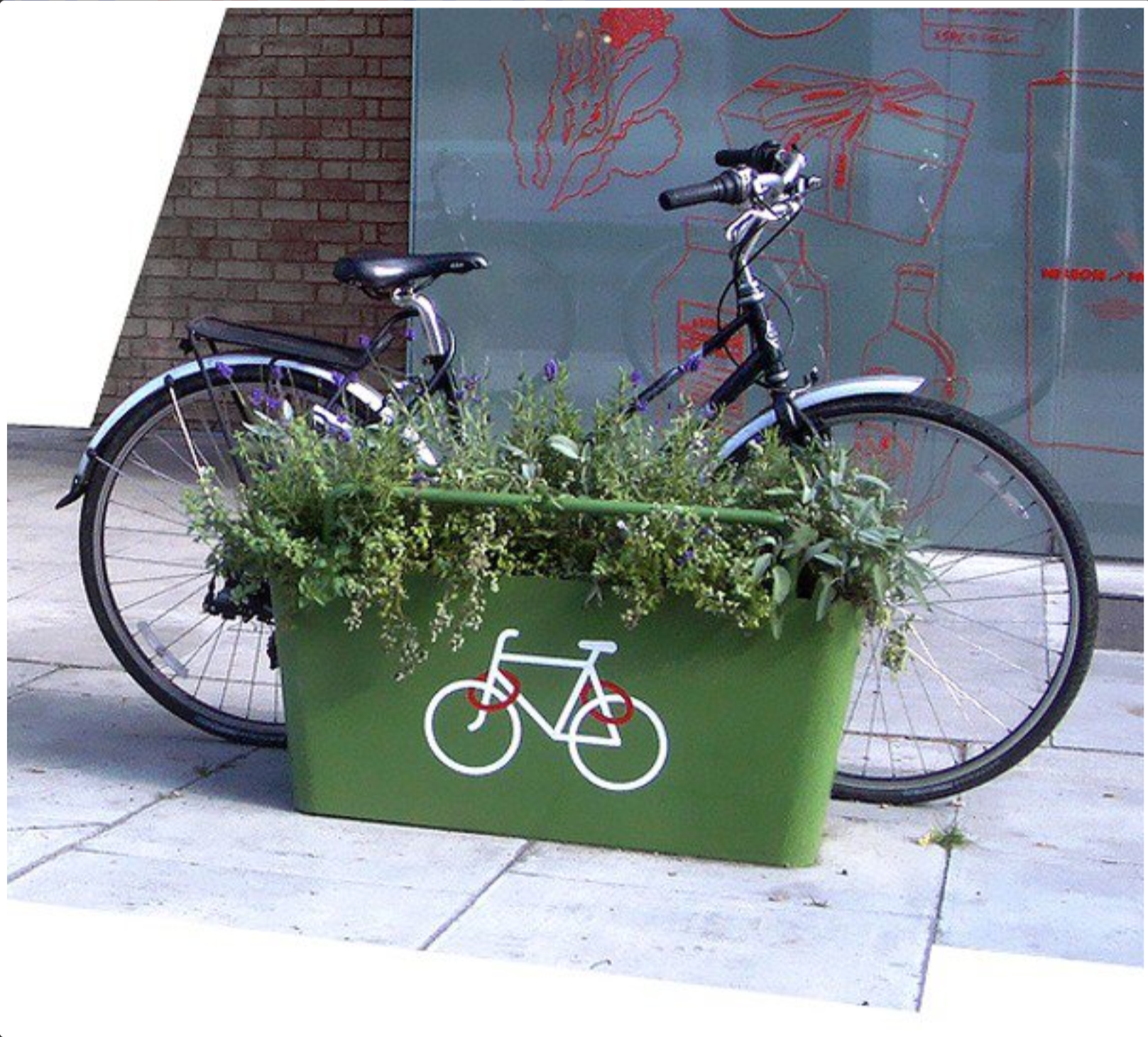 A bike leaning up against a green plant pot with a bike symbol on it, in front of a building