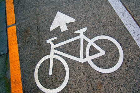 A bicycle symbol and an arrow painted on the road in white paint next to a yellow line on one side and a white line on the other side