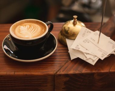 A cup of coffee next to a brass reception bell and a pile of receipts on a metal spike.