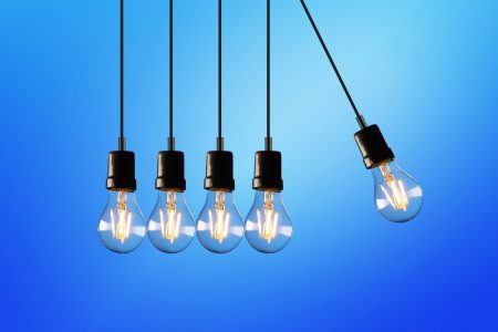 Five lights bulbs hanging against a blue background, one swinging away from the others